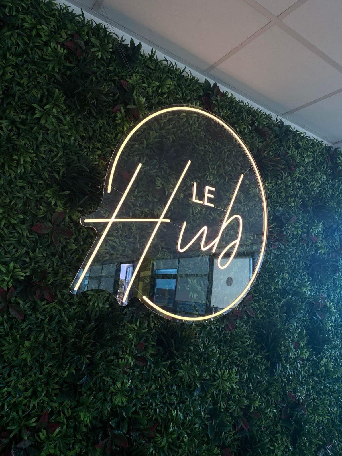 Logo néon blanc chaud Le Hub sur mur végétal
